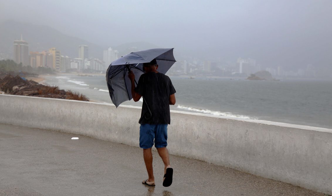 25 de Junio del 2020 Acapulco, Guerrero. Un hombre camina cubriéndose de las lluvias de ayer, de fondo la bahía de Acapulco. Foto: Carlos Alberto Carbajal