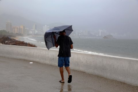25 de Junio del 2020 Acapulco, Guerrero. Un hombre camina cubriéndose de las lluvias de ayer, de fondo la bahía de Acapulco. Foto: Carlos Alberto Carbajal